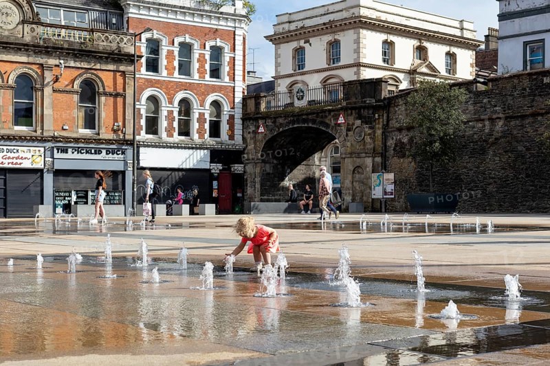 Child playing at the fountain in a square surrounded by historic buildings, Londonderry