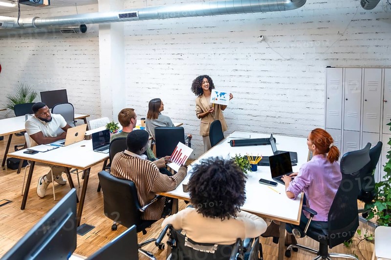 Woman showing graphs and data during coworking meeting with diverse young people in a modern coworking space