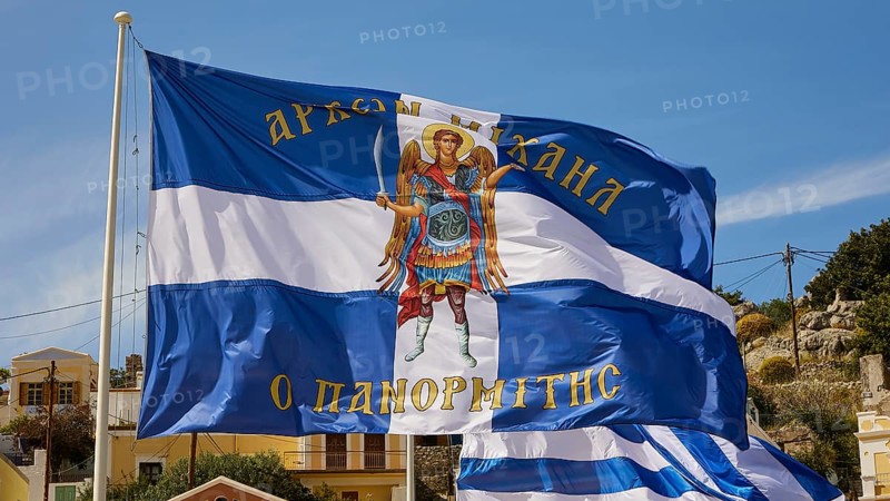 Flag with the Archangel Michael, Greek flag with an angel on a blue and white background on a sunny day, Symi town, Symi, Dodecanese, Greek Islands, Greece