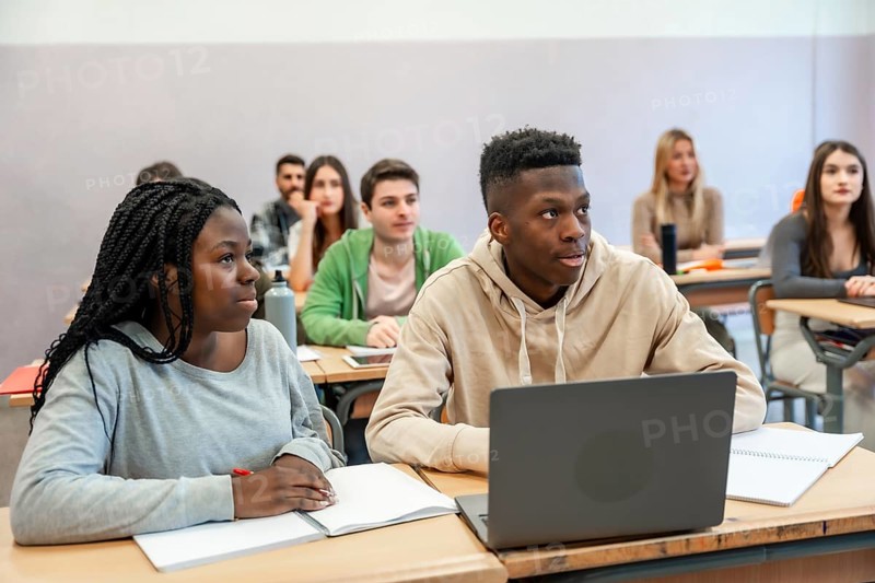 Multi ethnic students listening to lesson in university classroom, using laptop and taking notes