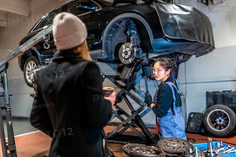 Professional female mechanic explaining car repair processes to a customer in a busy auto repair shop, fostering trust and satisfaction