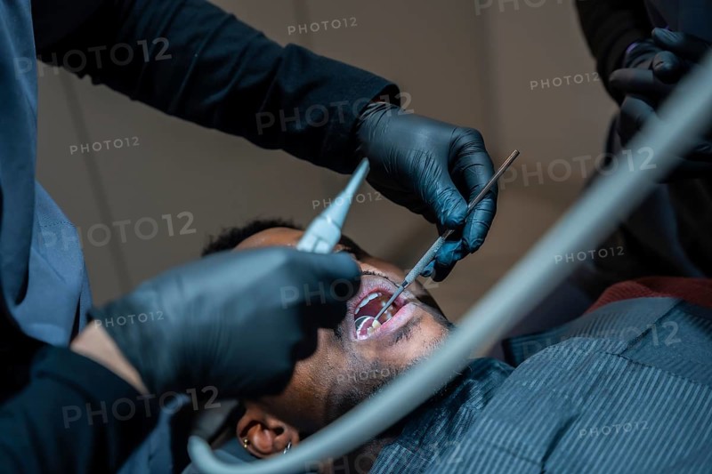 Dentist wearing black gloves examining patient's teeth with dental instruments during checkup in modern dental clinic