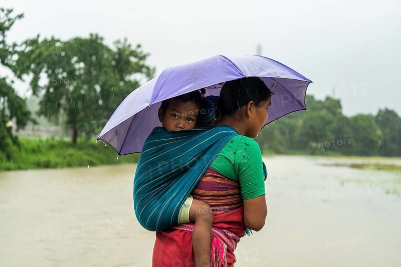 A tribal woman with her child stands with umbrella during a heavy rain in Golapara, India on 31 May 2025