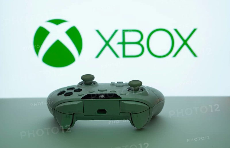 Dhaka, Bangladesh- 09 May 2025: A close-up of a white gamepad with the XBOX seen on screen in the background