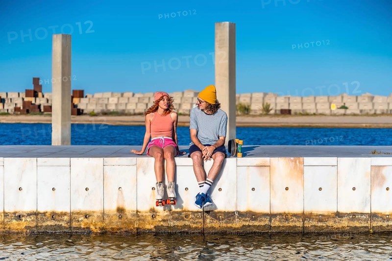 Young skaters enjoying a sunny day at the pier, talking and relaxing by the water with roller skates and skateboard