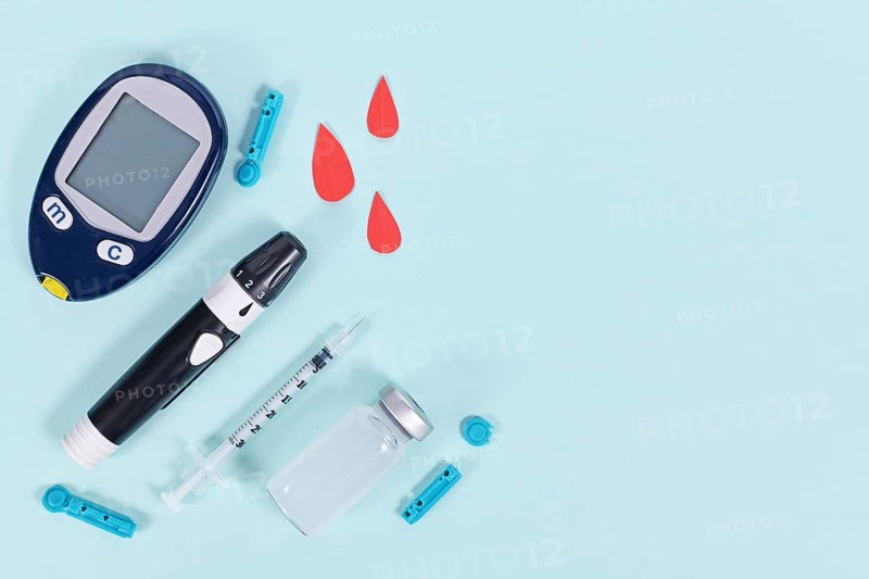 Diabetes treatment equipment with blood glucose sugar meter, lancet, insulin vial and syringe on blue background