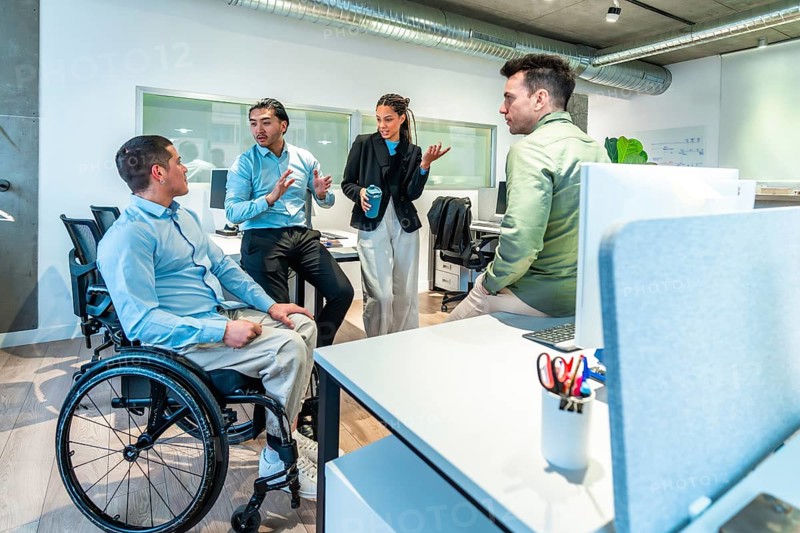 Business team discussing during a meeting in a modern office, with a disabled colleague actively participating in the conversation