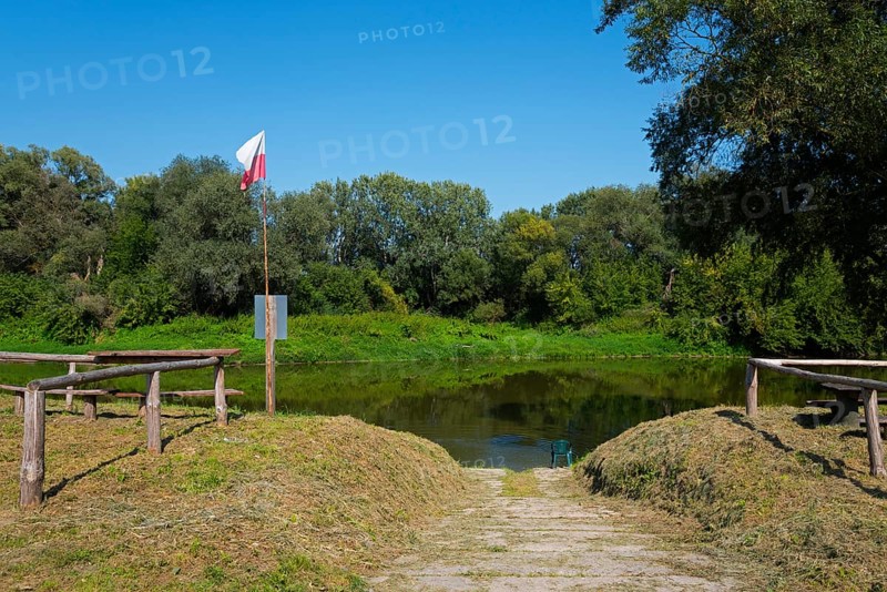 Riverbank with Polish flag and wooden railing, surrounded by green vegetation, bow River, border with Ukraine, Bereznica, Bereznica, Dorohusk, Horodlo, Horodlo, Hrubieszowski Voivodeship, Lublin Voivodeship, Poland