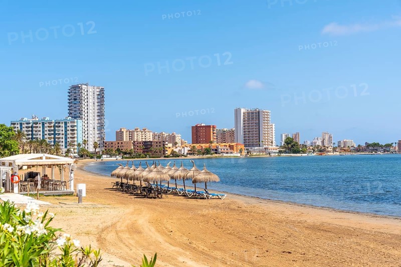 Tranquil beach scene with straw umbrellas and lounge chairs, overlooking the cityscape of la manga on the mar menor in murcia, spain, Playa de Cavanna