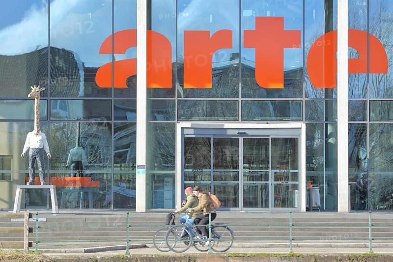 Entrance to the modern building of the ARD and ZDF broadcasting station Arte with sculpture Giraffe Man Sculpture Giraffe Man by Stephan Balkenhol, giraffe figure, giraffe man, animal figure, man figure, giraffe neck, mythical creature, cyclist, inscription, television station, broadcasting, Strasbourg, Bas-Rhin, Alsace, France