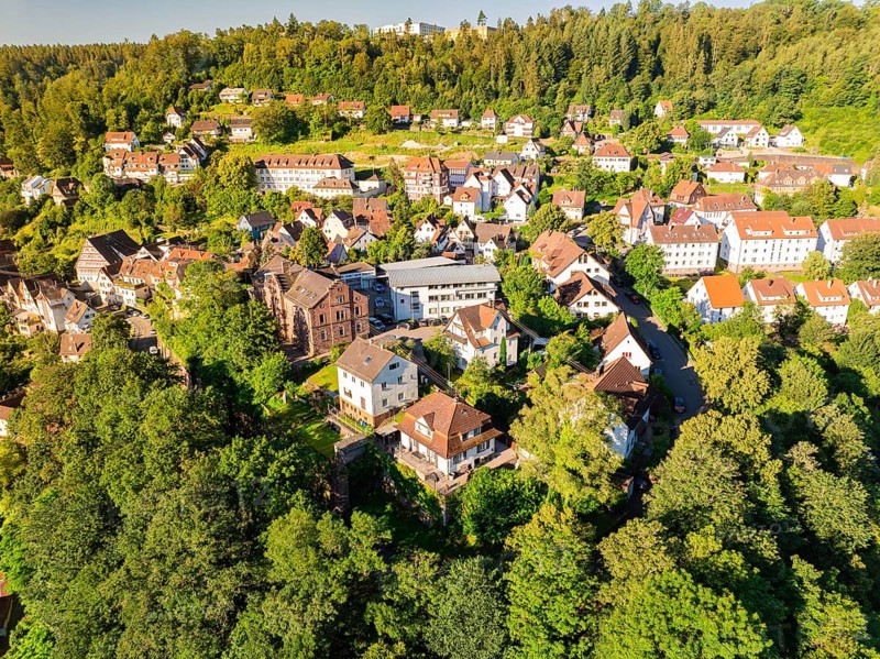 Aerial view of a settlement with many houses on a green hill on a sunny summer day, Calw, Black Forest, Germany