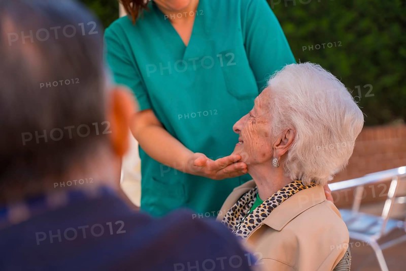 An older or mature woman with the nurse in the garden of a nursing home in a moment of love and affection caressing the face