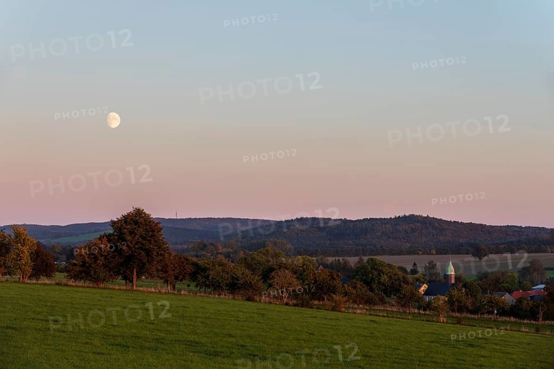 Evening mood with moon, the hills of the Upper Lusatian Highlands and the village church of Langenwolmsdorf, Stolpen, Saxony, Germany
