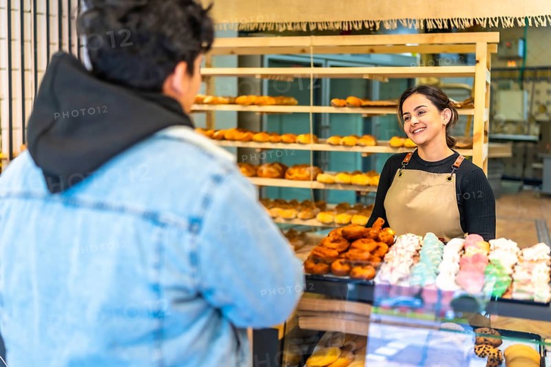 Rear view of a latin man buying in an artisan bakery attended by friendly saleswoman