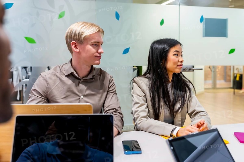 Two business professionals engaged in listening to a speaker during a meeting held in a modern coworking office space filled with light