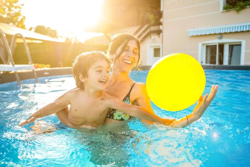 Mother and son having fun playing with a yellow inflatable ball in a swimming pool during a sunny summer vacation day
