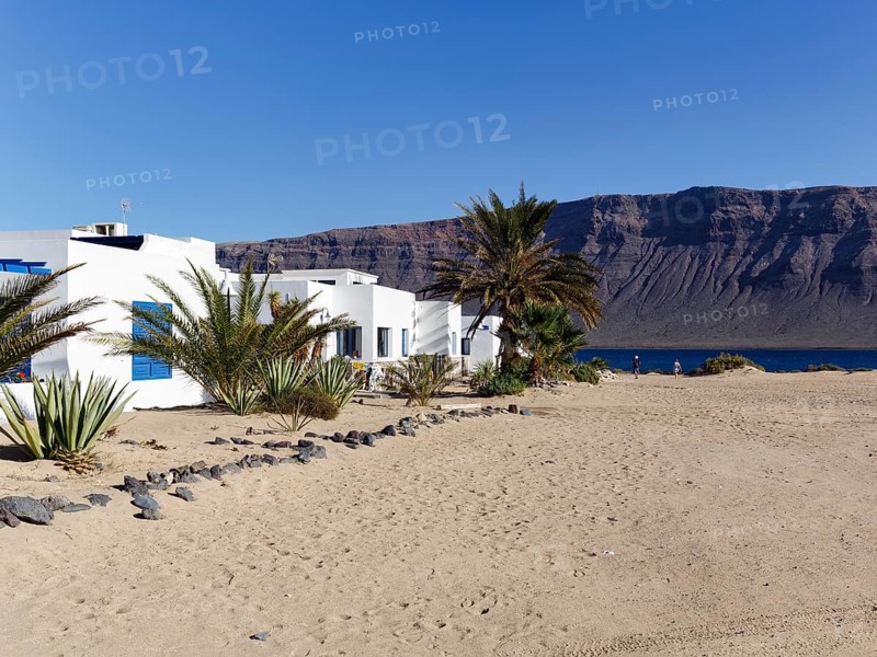 White holiday homes, palm trees on a sandy beach, Risco de Famara cliffs, Caleta del Sebo, La Graciosa Island, Chinijo Archipelago, Spain