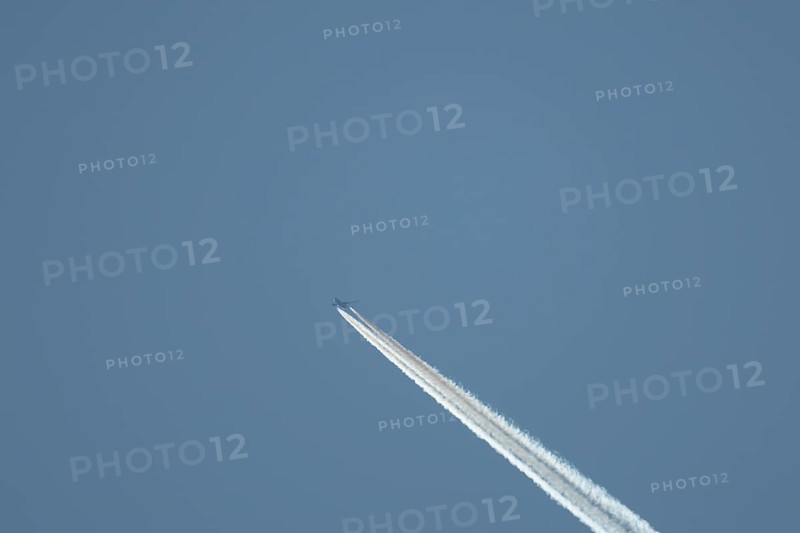 Boeing 777 aircraft flying across a blue sky leaving a contrail or vapor trail in the atmosphere behind the plane, England, United Kingdom