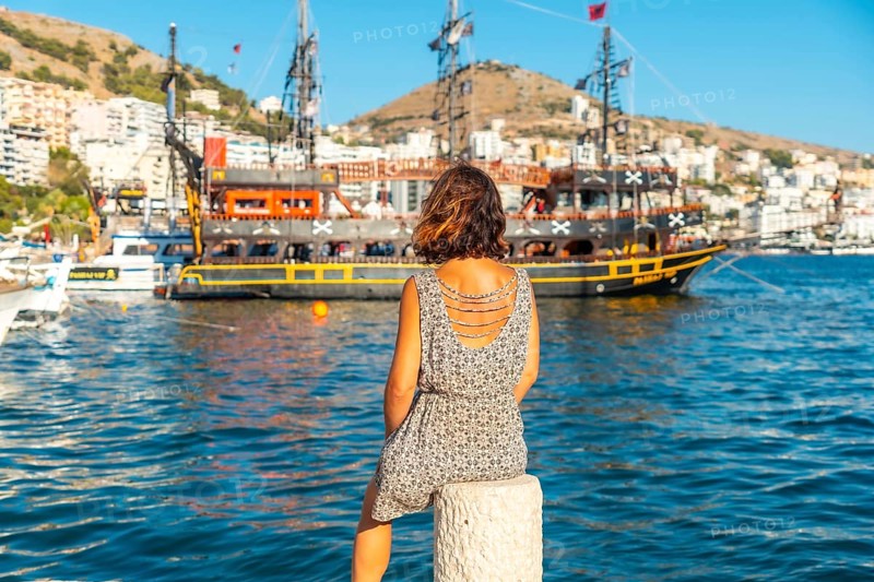 Woman looking at tourist boats at Saranda Beach on the Albanian Riviera in Sarande on Bulevardi Hasan Tahsini, Albania