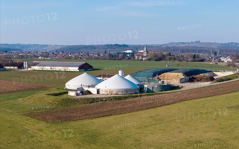 Biogas plant surrounded by fields, with buildings and village in the background on a slight hill, near Backnang, Rems-Murr-Kreis, Baden-Württemberg, Germany