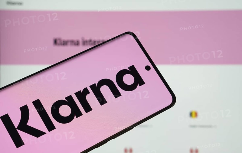 The logo of the klarna is displayed on a smartphone screen, and the website klarna is visible on a computer screen in the background