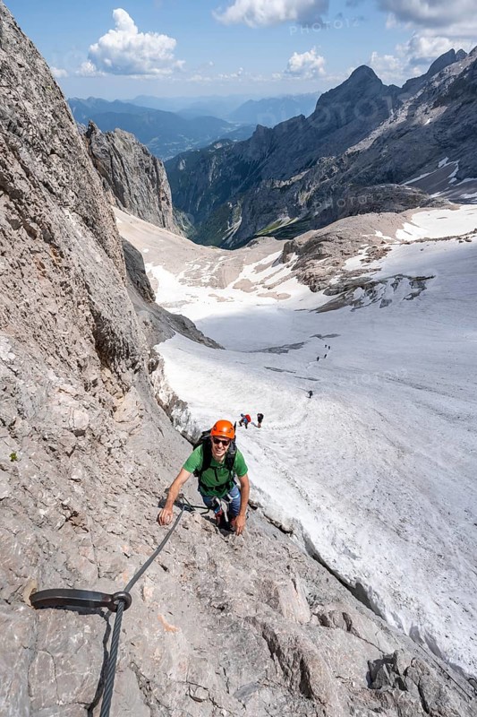 Mountaineer with helmet in a secured via ferrata, Zugspitz via ferrata, ascent to the Zugspitze, behind snowfield of the Höllentalferner and Höllental, Wetterstein range, Bavaria, Germany