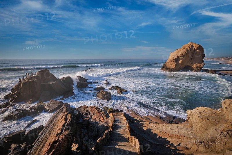 Penedo do Guincho stands majestically at Praia da Santa Cruz as ocean waves crash against it, creating a stunning sunset scene