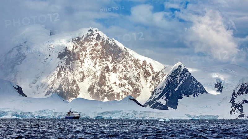 A ship sails along snow-covered mountains, surrounded by ice and clouds, in a cold and dramatic landscape, cruise ship in Antarctica