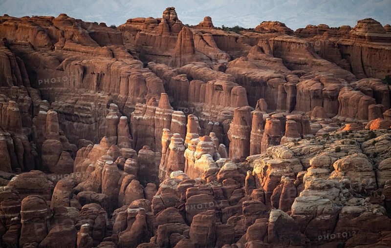 Stunning view of the unique rock formations in Arches National Park, Utah. The late afternoon sun casts warm hues over the rugged landscape, highlighting the natural beauty of the sandstone structures