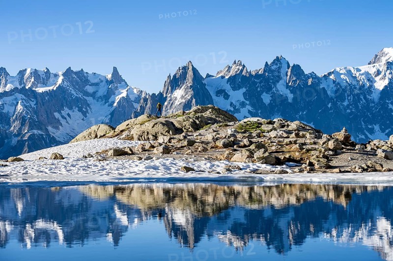 Young man in front of impressive mountain landscape in morning light, reflection in the Lac Blanc mountain lake, mountain summit, Aiguille Verte, Grandes Jorasses, Aiguille du Moine, Mont Blanc, Mont Blanc Massif, Chamonix-Mont-Blanc, Haute-Savoie, France