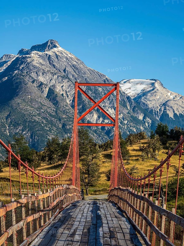 Old-style orange suspension bridge, river Rio Nadis south of Cochrane, mountain range at Rio Baker in the back, Patagonia, Chile