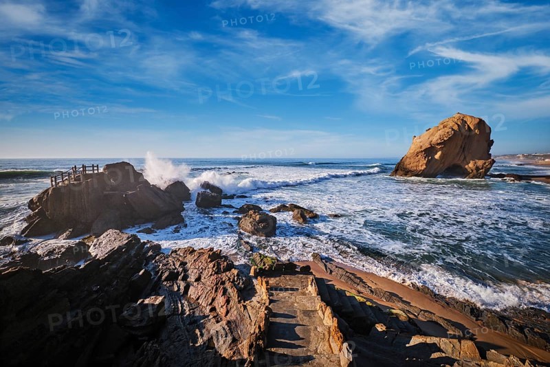 Penedo do Guincho rock arch stands majestically as ocean waves crash on the sandy beach during sunset at Praia da Santa Cruz