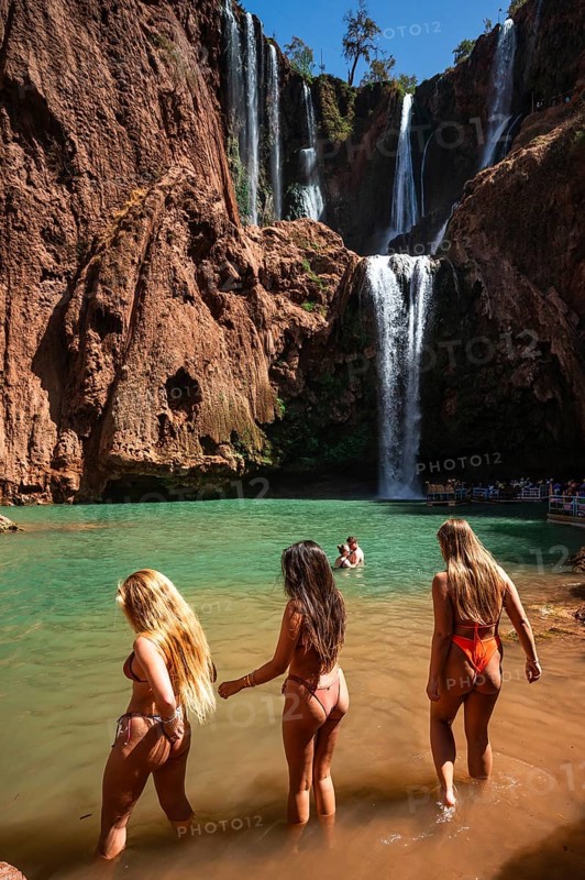 OUZOUD, MOROCCO - OCTOBER 5, 2024: Three beautiful women in bikinis enter the water under the waterfall Ouzoud