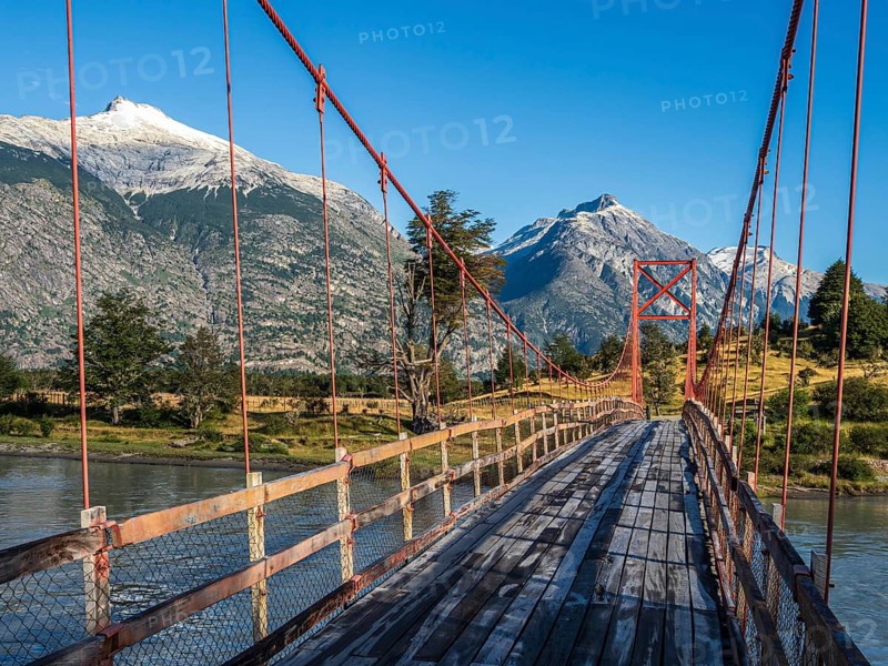 Old-style orange suspension bridge, river Rio Nadis south of Cochrane, mountain range at Rio Baker in the back, Patagonia, Chile