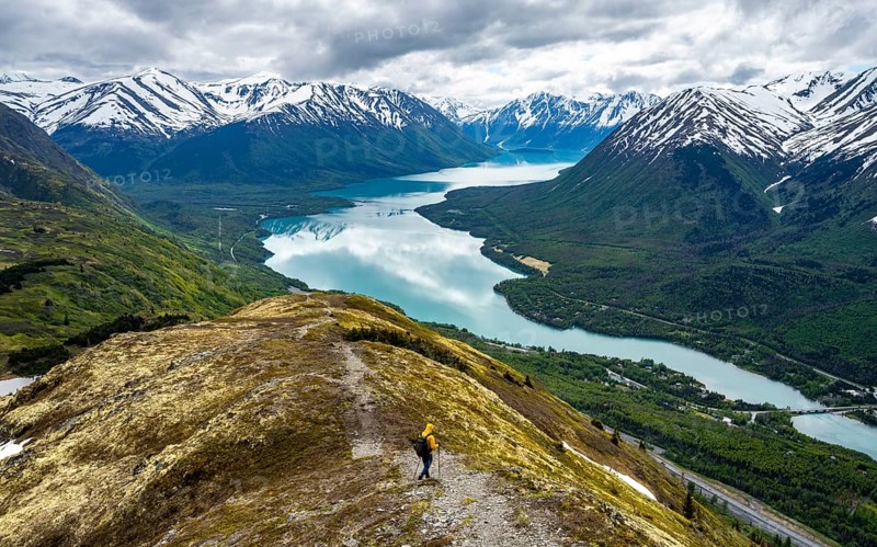 Climbers on a hiking trail on Slaughter Ridge, views of snowy mountains in spring and turquoise Lake Kenai Lake, Cooper Landing, Kenai Peninsula, Alaska, USA