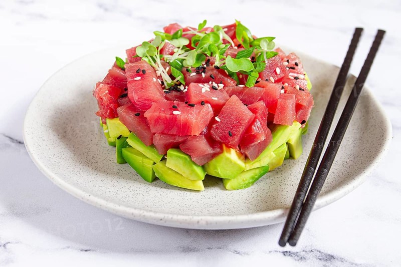 Fresh tuna tartare with avocado served on a marble table with soy sauce and seaweed salad