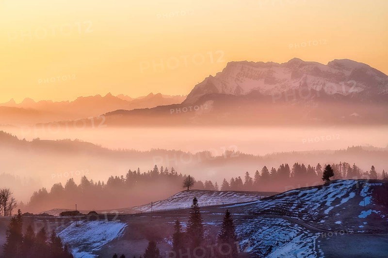 Misty morning atmosphere over hilly landscape with views of Mount Pilatus and Prealps, Entlebuch, Canton of Lucerne