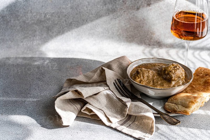 A bowl of satsivi, the renowned Georgian chicken in walnut sauce, paired with freshly baked bread and a glass of rare amber wine, presented elegantly on a minimalist table setting