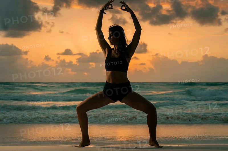 A woman gracefully performs yoga on a sandy beach, silhouetted against a stunning sunset, with waves gently lapping the shore, embodying peace and mindfulness in Mexico