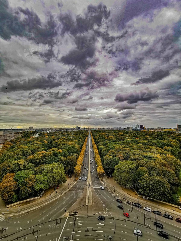 A central avenue in Berlin surrounded by autumnal forests under a dramatic sky, view from the Victory Column, Berlin