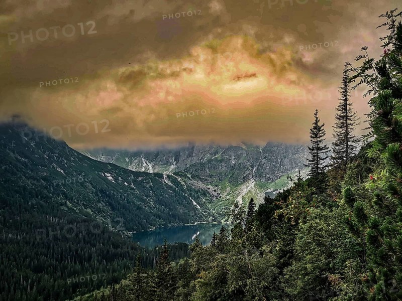A mountain lake, Morskie Oko, surrounded by forests under a dramatic sky at dusk, view over Morske Oko, in the High Tatras National Park, Poland