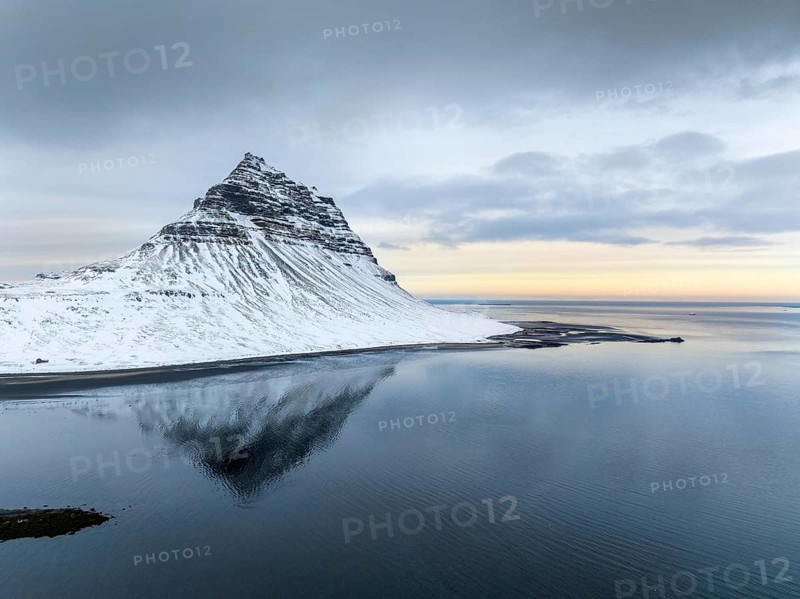 Kirkjufell Mountain rises majestically, its snow-capped peak mirrored perfectly in tranquil waters below. A serene winter landscape in Iceland, captivating with its natural beauty