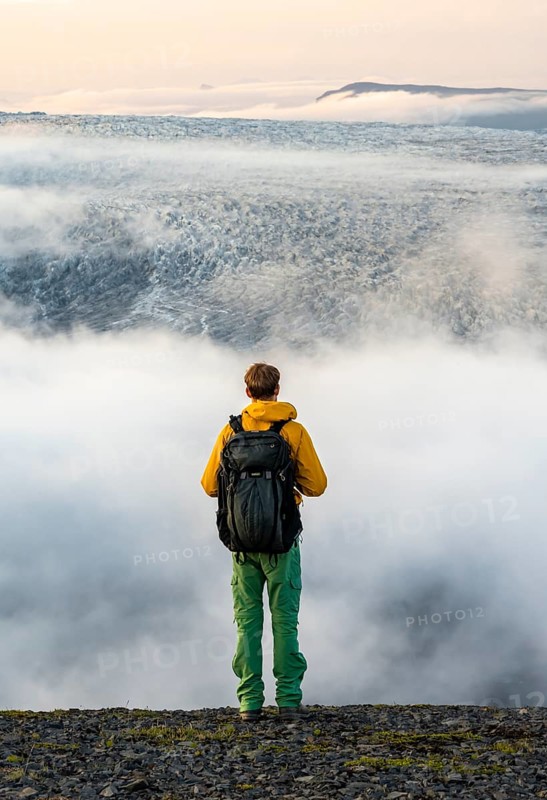Young man in front of impressive landscape at sunset, fog, clouds moving around, glacier ice of the glacier tongue Kötlujökull, glacier Myrdalsjökull, Pakgil, Iceland