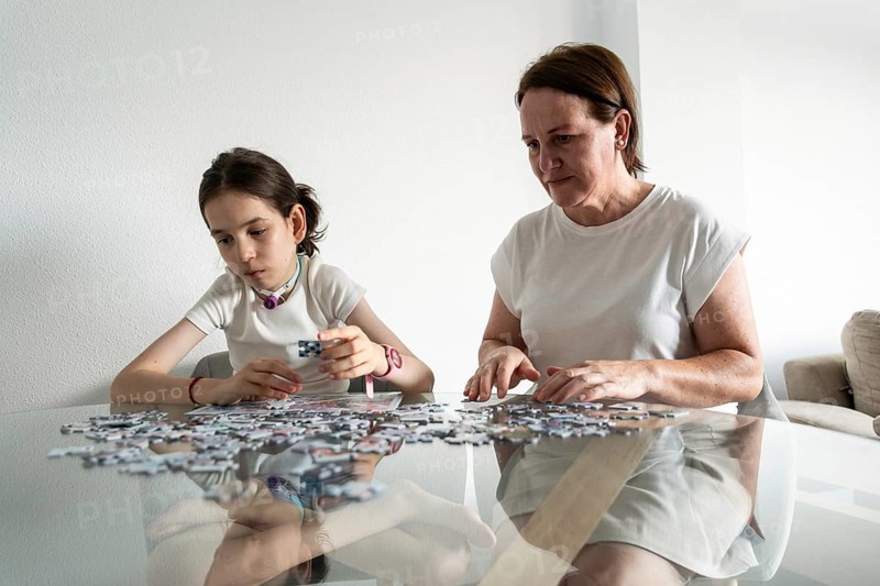 A mother and daughter, who has a tracheostomy, enjoy quality time together solving a puzzle at the dining table. They demonstrate warmth, connection, and the supportive atmosphere of family life