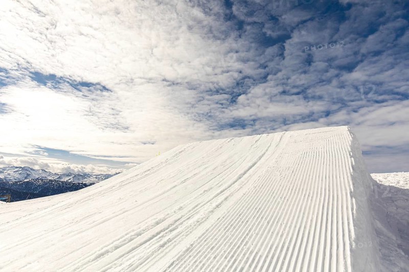 Breathtaking snowy mountain landscape under a vibrant blue sky, accentuated by scattered clouds. The pristine snow creates a serene and picturesque winter scene