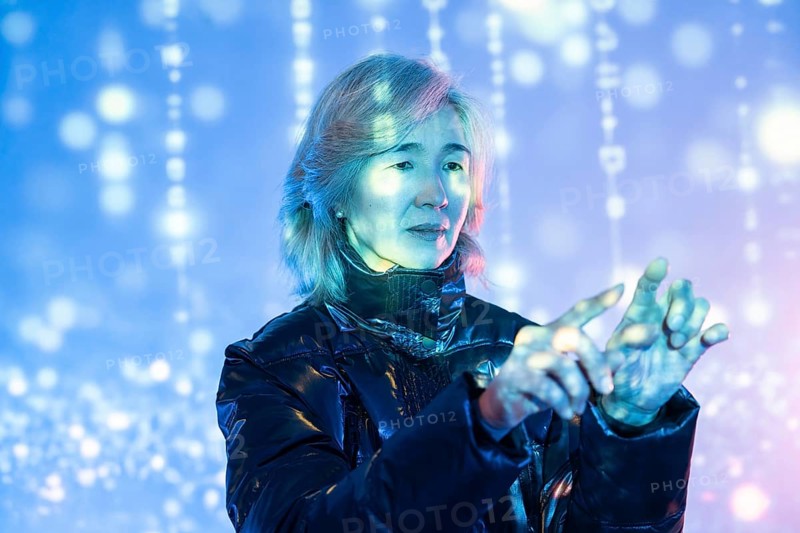 An elderly Asian woman navigates a vibrant virtual metaverse environment, showcasing the intersection of technology and age as she interacts with digital elements around her