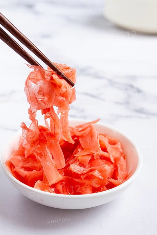 Pickled ginger, with chopsticks, in a small white bowl, on a marble countertop, close-up, no people