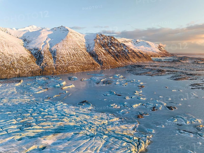 A breathtaking aerial view of Skaftafell's Glacier, showcasing its icy expanse amidst snow-capped mountains under a serene winter sky, capturing nature's pure beauty