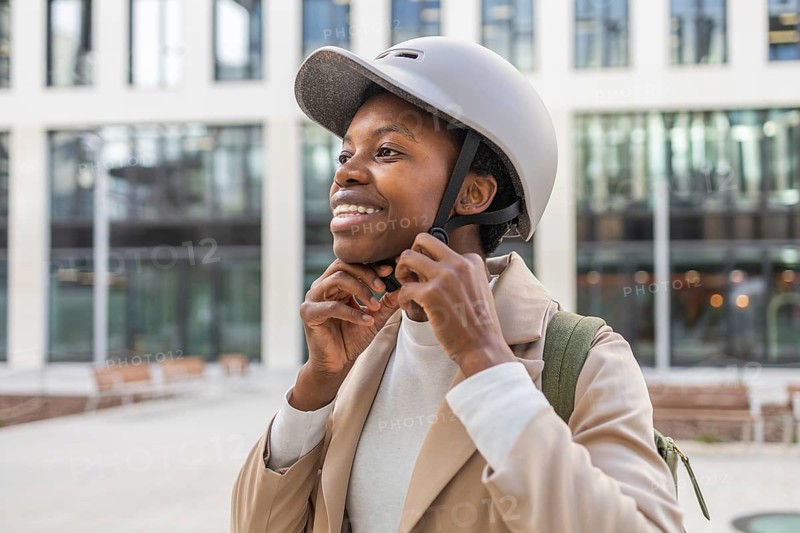 A confident black woman adjusts her helmet, standing amidst modern urban architecture She embodies a mix of style and safety in a bustling city setting