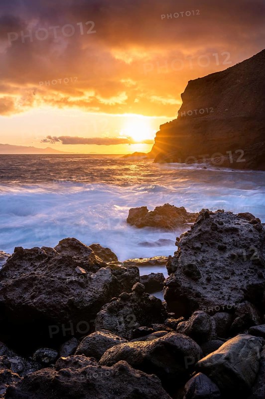 Sunrise on the beach at San Marcos. Rocks, sea and the sun. Tenerife in the background. Long exposure. Bright clouds in the sky. La Gomera, Canary Islands, Spain